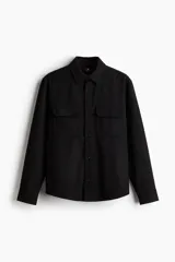 Sobrecamisa negra de corte recto, con cuello clásico, cierre frontal con botones, dos bolsillos de parche con solapa en el pecho, mangas largas con puños abotonados y bajo redondeado.