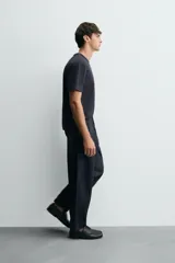 Pantalón de denim azul oscuro, corte wide fit, largo cropped, con pliegues frontales, bolsillos laterales y traseros asimétricos. Cierre frontal con cremallera y gancho metálico oculto.
