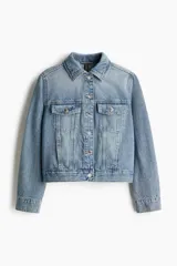 Campera trucker corta de denim celeste, con cuello clásico, cierre frontal con botones metálicos, mangas largas con puños abotonados, bolsillos superiores con solapa y botón, bolsillos laterales y trabillas ajustables con botones en los laterales del bajo.