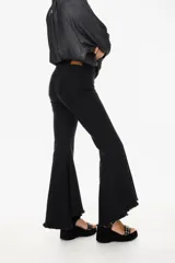 Pantalón de jean negro elastizado con corte ajustado y volados en la parte baja de la pierna. El ruedo es más largo en la parte trasera y tiene terminación descosida.