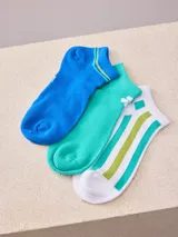 Pack de tres pares de medias de algodón a la altura del tobillo. Un par es de color azul con detalles en amarillo y verde, otro par es de color verde con un pequeño estampado de una flor y el tercer par es blanco con rayas verticales verdes.