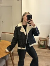 Campera gamulán negra con interior de piel sintética color crema, cierre cruzado con cremallera y cuello con solapas amplias.