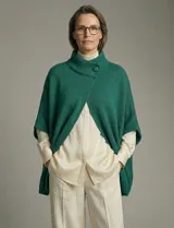 Capa o poncho tejido color verde esmeralda, con cuello polera alto que se cierra con un botón grande en el lateral. Presenta mangas cortas estilo japonesa y un calce amplio.