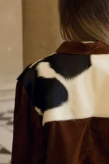 Chaqueta marrón de cuero vacuno con canesú delantero y trasero en cuero vacuno raza Holando (blanco con manchas negras), con cuello clásico, cierre frontal con botones y bolsillos laterales.