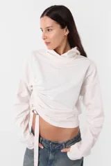 Buzo blanco de rústico, con capucha forrada y detalle de tira para frunce y hebilla en delantero. Mangas con recortes y mitón para dedo pulgar.