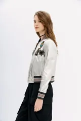 Campera bomber de cuero ovino color plateado, con cuello, puños y ruedo de ribb metalizado. Presenta apliques de parches bordados con lentejuelas y mostacillas.
