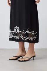 Maxi vestido negro de breteles finos con escote recto y bordado floral en el ruedo.