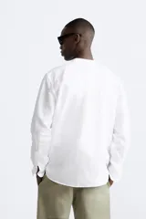 Camisa color beige claro, de corte relaxed fit, confeccionada en tejido de lino y algodón. Tiene cuello mao, manga larga con puños abotonados y cierre frontal con botones.