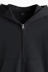 Campera con capucha en felpa de algodón pesado, color negro, con cierre y bolsillos delanteros, hombros caídos y corte oversized.