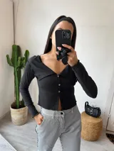 Remera negra de tejido de punto acanalado, con cuello polo, cierre frontal con botones y mangas largas.