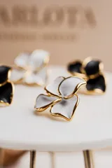 Par de aros tipo botón con forma de flor abierta, con pétalos blancos y borde dorado.