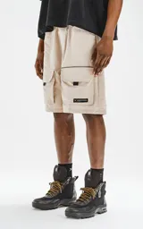 Bermuda color beige con cintura elástica, cordón de ajuste y cinturón negro con hebilla plástica. Tiene bolsillos delanteros y bolsillos cargo con solapa.