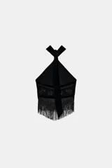 Top halter negro con cuello ajustable anudado, escote halter y hombros descubiertos. Presenta un panel central de terciopelo y apliques de abalorios brillantes en la parte delantera, con bajo asimétrico terminado en flecos largos.
