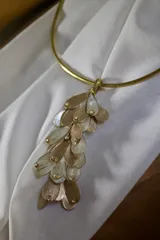 Gargantilla rígida dorada con dije colgante de pétalos dorados y blancos con incrustaciones de strass.