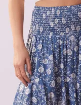 Falda midi de algodón estampada con flores blancas sobre fondo azul. Tiene pretina ancha elastizada en punto smock, ruedo con volados y forro interno a tono.