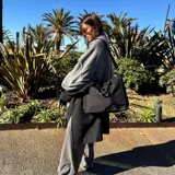 Bolso tipo tote color gris claro, con doble asa de mano y correa larga regulable. Tiene dos bolsillos laterales y un bolsillo frontal.