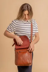 Bandolera de hombro color gris claro, con solapa frontal y correa ajustable. Presenta un diseño simple y práctico, ideal para uso diario.