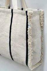 Bolso tipo tote tejido a mano, color crudo con rayas verticales negras y flecos en los laterales.