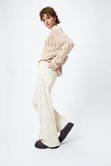 Pantalón de denim blanco con calce wide leg y ruedo desflecado. Presenta tachas metálicas a lo largo de los laterales.
