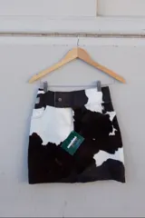 Falda corta confeccionada a mano en cuero ovino con estampado de vaca en blanco y negro. Presenta bolsillos delanteros y traseros, y un diseño de tiro medio con cierre de botón.