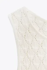 Vestido corto sin mangas, color blanco roto, confeccionado en tejido de punto con diseño calado de rombos. Presenta cuello redondo con abertura y botón en la espalda.