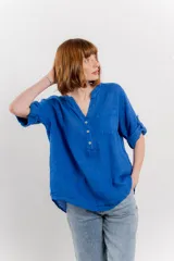 Camisa azul de lino con escote en V abotonado, bolsillo frontal y mangas 3/4 con trabilla.
