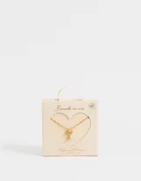 Cadena corta dorada con dije de moño con piedras de zirconia y dije de corazón colgante.