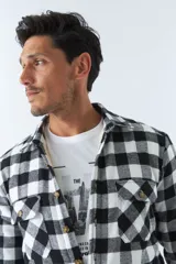 Sobrecamisa de algodón para hombre con interior de corderito, estampado a cuadros en tonos negro, blanco y azul. Tiene cierre de botones, bolsillos tipo cartera y logo en goma. El modelo usa talle M.