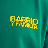 Buzo verde oscuro con cuello redondo, puños y cintura acanalados. Estampado amarillo en el pecho con la frase "Barrio y Familia".