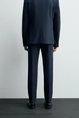 Pantalón de vestir azul marino, de corte slim fit, con bolsillos laterales y traseros. Se ajusta a la cintura con cinturón de cuero marrón.