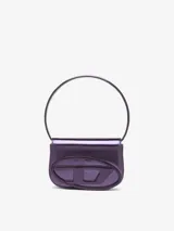 Bolso bandolera Diesel modelo 1DR, color violeta metalizado, con asa corta rígida y correa larga extraíble. Presenta solapa con cierre magnético y logo ovalado "D" en relieve.