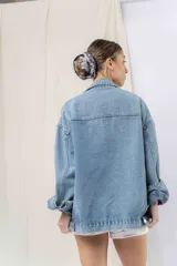 Campera denim celeste de corte oversize, con cuello clásico, cierre frontal con botones metálicos, bolsillos delanteros con solapa, bolsillos laterales y mangas largas con puños abotonados.