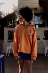 Buzo naranja de algodón con cuello en V y bordado en el frente. Tiene mangas largas con puños y ruedo acanalados.