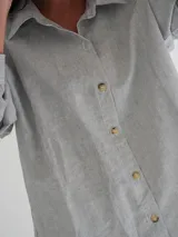 Camisa celeste a rayas verticales finas, con cuello clásico, cierre frontal con botones y mangas largas. Presenta bordados de un sol, un caballo y líneas horizontales en la parte superior de la espalda.