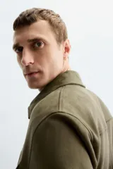 Sobrecamisa color beige de tejido efecto ante, corte regular fit, con cuello solapa, manga larga con puños abotonados, bolsillos de parche con solapa en el pecho y bolsillos de ojal en la cadera.