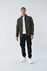 Campera de sherpa verde con detalles en negro, cuello alto, cierre frontal y bolsillo con cierre en el pecho.