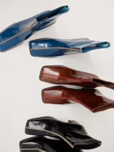 Botas de cuero charol negro con caña media y punta cuadrada. Cuentan con cierre trasero, tirador y bordado contrastante en el empeine. El taco es de madera y la suela de goma.