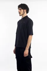 Remera polo negra de manga corta con cierre dorado en el cuello y logo bordado en el pecho.