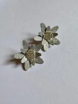 Par de aros plateados con forma de flor y centro dorado con textura.