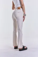 Pantalón jean color crudo, de corte recto y tiro medio, con tachas plateadas en los laterales. Sin lycra.