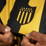 Camiseta de fútbol Puma del Club Atlético Peñarol, modelo Home, con franjas verticales amarillas y negras. Incluye logo Puma y escudo del club con cinco estrellas.