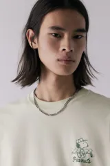 Remera color crema de corte holgado, con cuello redondo y estampado pequeño de Snoopy y la frase "Peanuts" en el pecho.