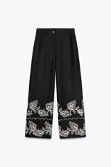 Pantalón culotte negro de lino y viscosa con bordados florales en el ruedo. Tiene tiro medio, cintura con trabillas, bolsillos laterales y cierre frontal con cremallera y botón.