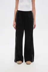 Pantalón deportivo negro de corte ancho y tiro alto, con cintura elástica y cordón ajustable. Presenta una raya blanca vertical a cada lado.