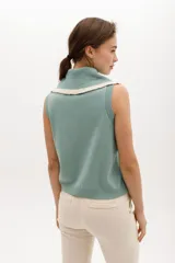 Chaleco de punto sin mangas, color azul marino, con cuello y frente adornados con volados en contraste de color blanco o crudo.