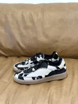 Zapatillas bajas con estampado de vaca en blanco y negro, con cordones negros y suela color caramelo.