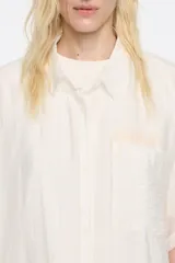 Camisa oversize blanca con rayas verticales finas en gris oscuro, cuello camisero, manga corta ancha, cierre frontal con botones y bolsillo de parche en el pecho. Confeccionada en viscosa y poliamida.