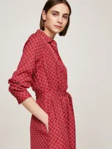 Vestido camisero midi rojo con estampado geométrico blanco, cuello camisero, manga larga con puños abotonados, cinturón anudable y abertura frontal.