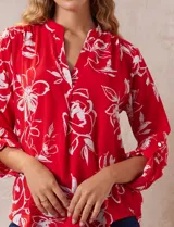 Blusa de gasa roja con estampado floral blanco, cuello a la base con escote en V y mangas 3/4 regulables con presilla y botón.
