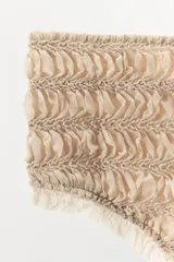 Mini shorts color beige confeccionados en tejido con estructura, tiro alto, cintura elástica y detalle de volantes a tono en los bordes.